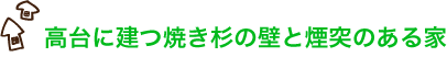 高台に建つ焼き杉の壁と煙突のある家